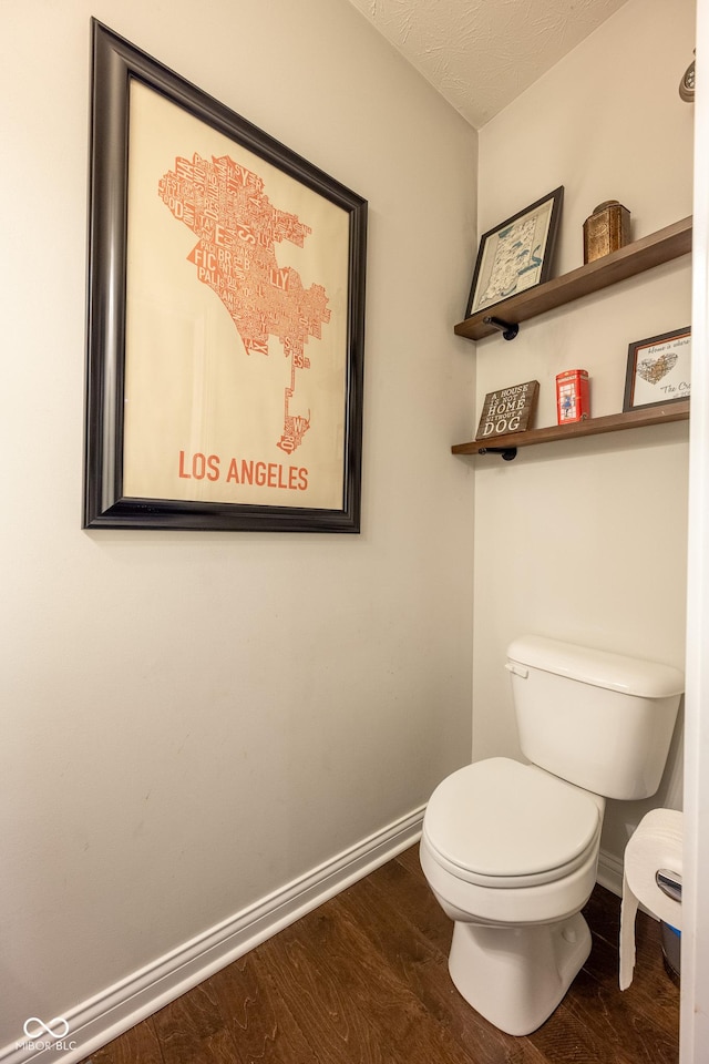 bathroom featuring baseboards, wood finished floors, and toilet