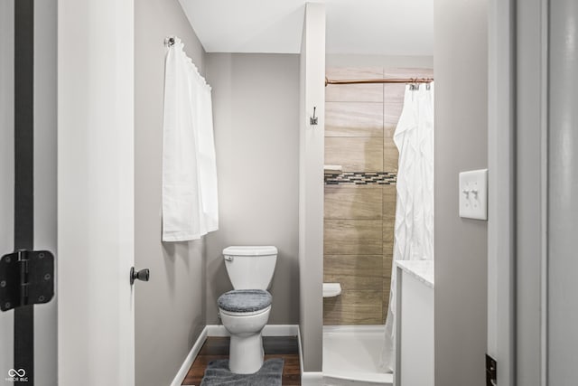 full bath featuring toilet, baseboards, a tile shower, and wood finished floors