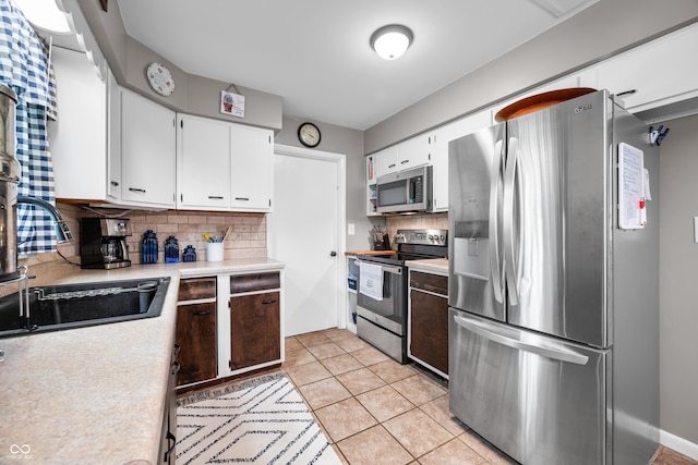 kitchen with backsplash, appliances with stainless steel finishes, light countertops, a sink, and white cabinets