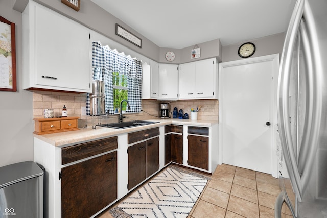 kitchen featuring decorative backsplash, stainless steel refrigerator, a sink, light countertops, and white cabinets