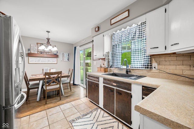 kitchen with a notable chandelier, a sink, light tile patterned floors, tasteful backsplash, and stainless steel refrigerator with ice dispenser