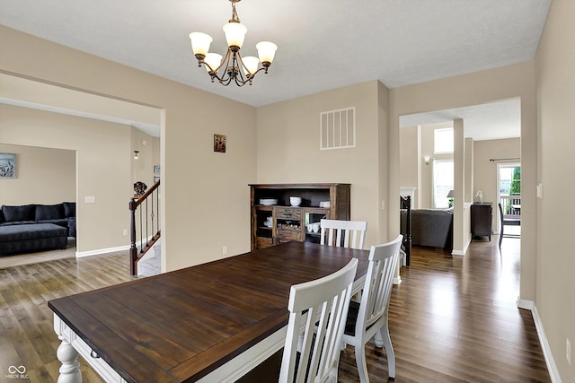 dining area featuring wood finished floors, a chandelier, stairs, and baseboards