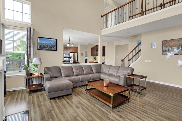 living area with a high ceiling, wood finished floors, baseboards, stairs, and a chandelier