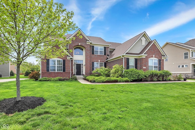 view of front of property featuring brick siding, a front lawn, and roof with shingles