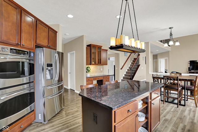 kitchen featuring stainless steel appliances, light wood finished floors, decorative light fixtures, glass insert cabinets, and recessed lighting