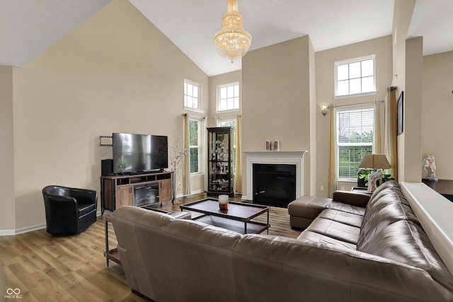 living room with a glass covered fireplace, high vaulted ceiling, wood finished floors, baseboards, and healthy amount of natural light