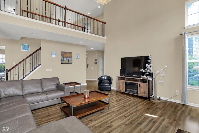 living area featuring a towering ceiling, wood finished floors, baseboards, stairs, and recessed lighting