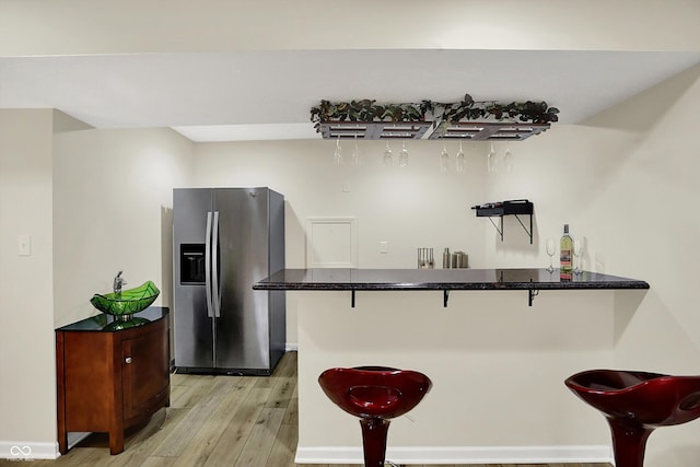 kitchen with stainless steel refrigerator with ice dispenser, a kitchen breakfast bar, light wood-style floors, and dark countertops