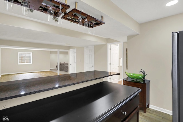 kitchen with light wood finished floors, baseboards, freestanding refrigerator, dark stone counters, and open floor plan