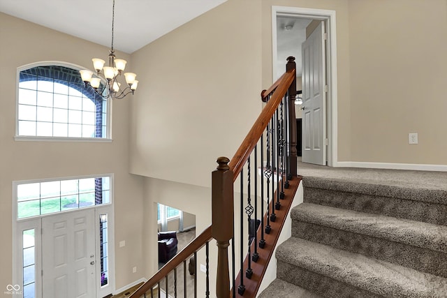 carpeted foyer featuring healthy amount of natural light, a chandelier, a high ceiling, stairs, and baseboards