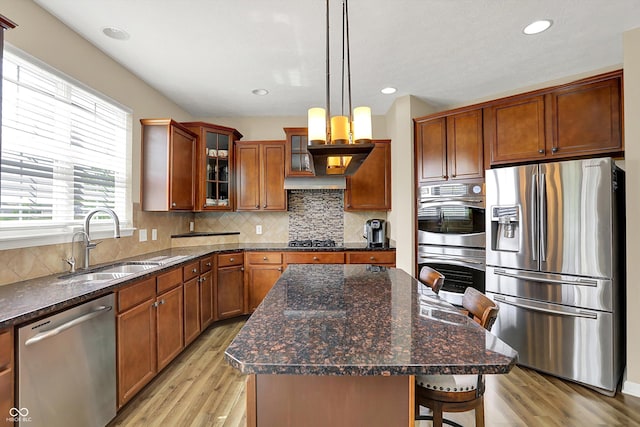 kitchen featuring stainless steel appliances, a sink, light wood-type flooring, brown cabinetry, and glass insert cabinets
