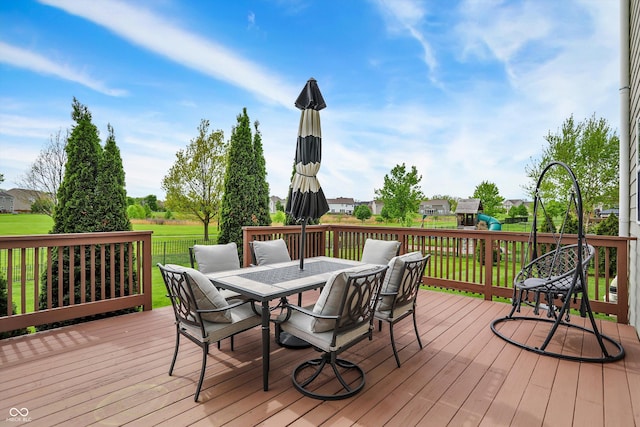 wooden deck featuring outdoor dining space, a yard, and a playground