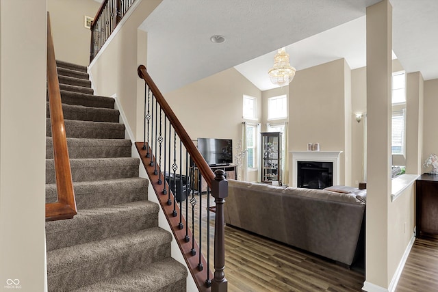 staircase with wood finished floors, high vaulted ceiling, baseboards, a chandelier, and a fireplace