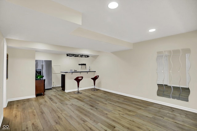 basement with stainless steel refrigerator with ice dispenser, wood-type flooring, baseboards, wet bar, and recessed lighting