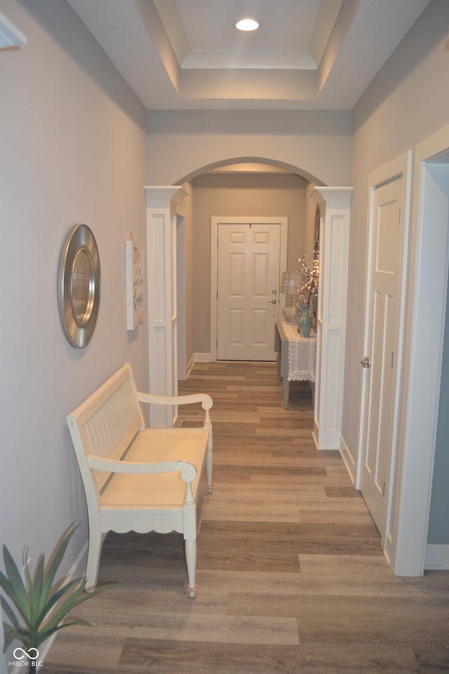 hallway featuring baseboards, arched walkways, a tray ceiling, and wood finished floors