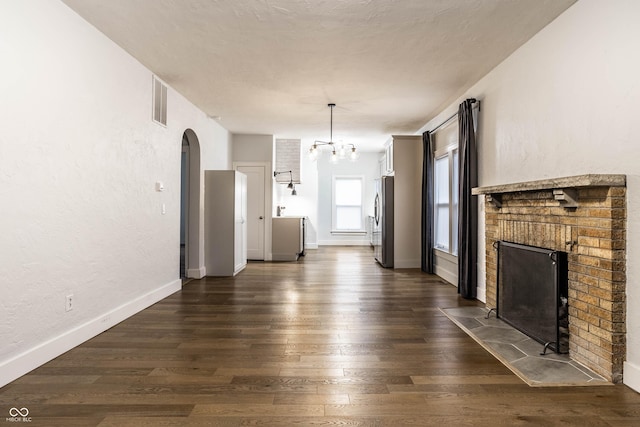 1451 N Grant Ave, Indianapolis, IN 46201 - unfurnished living room featuring a fireplace, arched walkways, dark wood-style flooring, a chandelier, and a textured wall