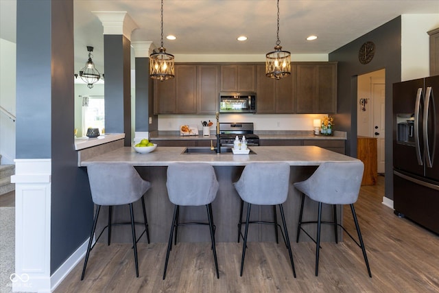 kitchen with dark brown cabinetry, a kitchen bar, pendant lighting, dark wood finished floors, and stainless steel appliances