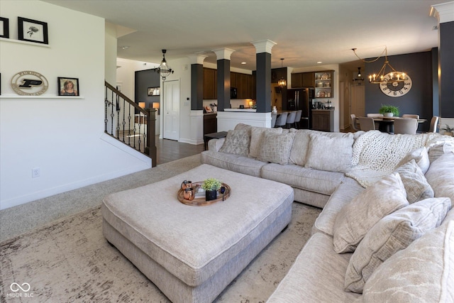 carpeted living room with stairs, decorative columns, baseboards, and a chandelier