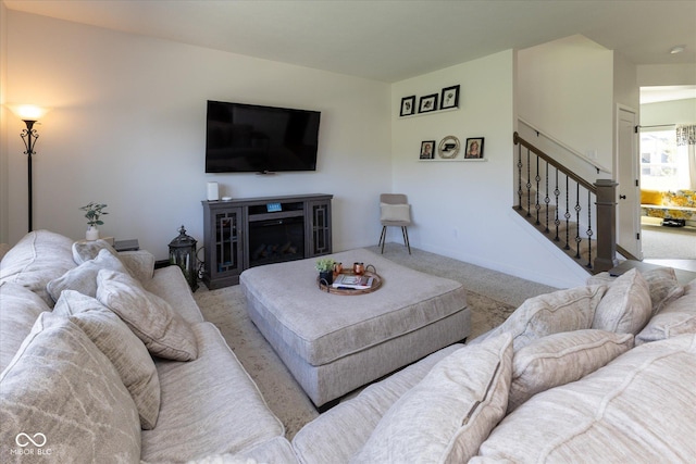 carpeted living area featuring a glass covered fireplace, baseboards, and stairs