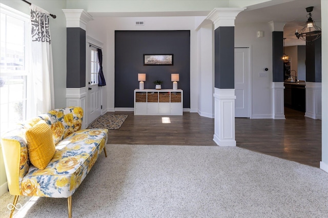 living room featuring visible vents, a decorative wall, wood finished floors, ornate columns, and a wainscoted wall