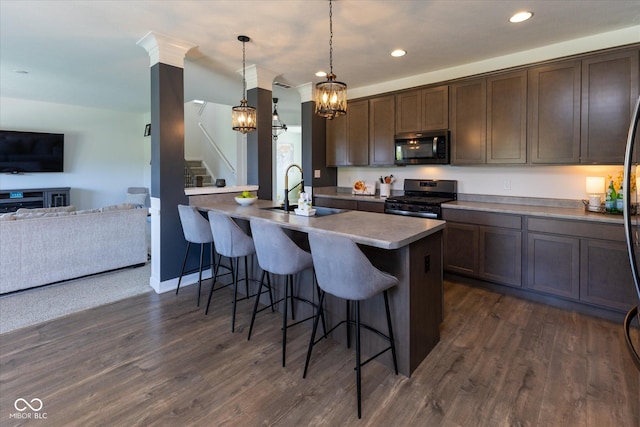kitchen featuring dark brown cabinetry, a breakfast bar, a sink, stainless steel appliances, and open floor plan