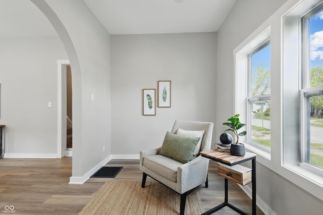 living area featuring arched walkways, visible vents, plenty of natural light, and wood finished floors