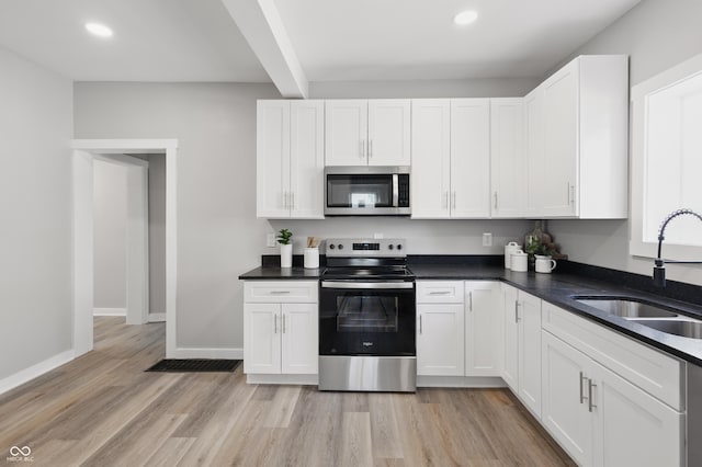 kitchen with appliances with stainless steel finishes, a sink, white cabinets, beamed ceiling, and light wood-style flooring