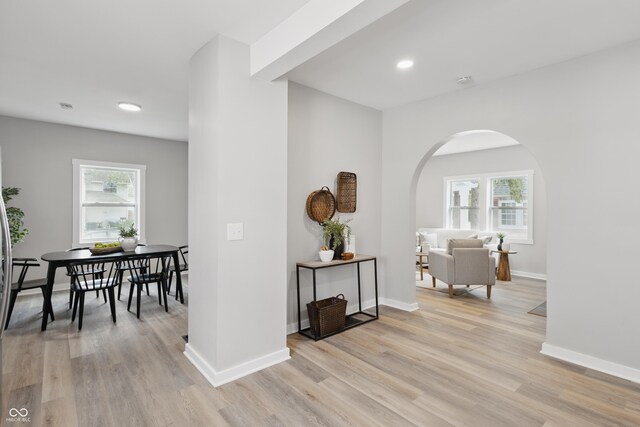 corridor featuring light wood-type flooring, arched walkways, baseboards, and plenty of natural light