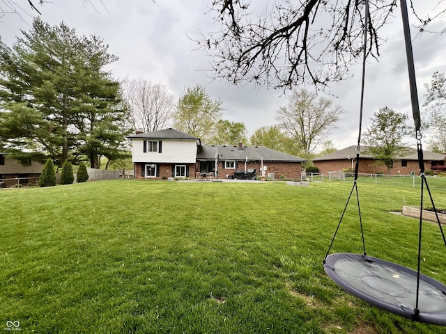rear view of property featuring fence, a lawn, and brick siding