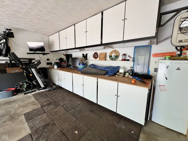 kitchen featuring a textured ceiling, freestanding refrigerator, concrete flooring, and white cabinetry