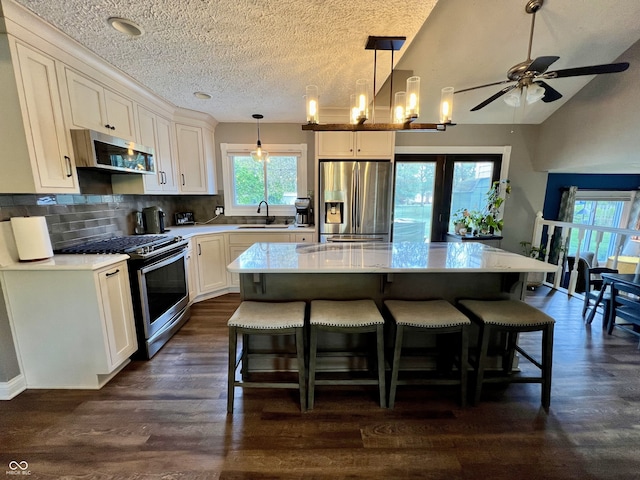 kitchen featuring decorative backsplash, a center island, a textured ceiling, a sink, and appliances with stainless steel finishes