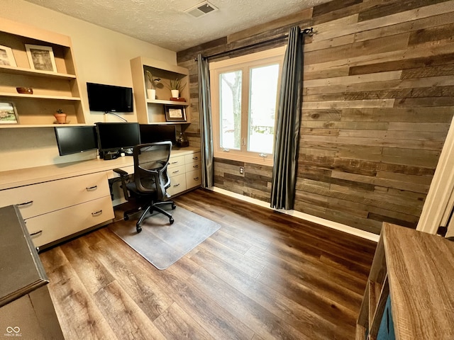 office space with visible vents, wood finished floors, wooden walls, a textured ceiling, and built in desk