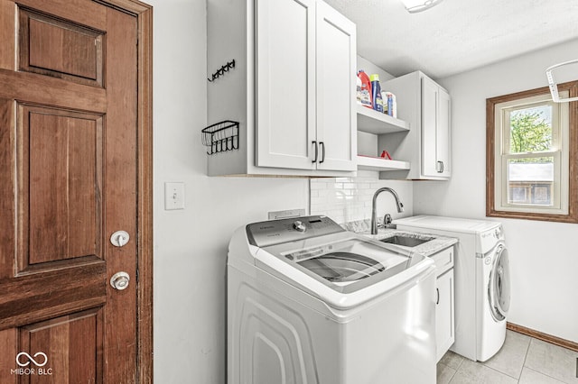 washroom featuring washing machine and dryer, cabinet space, a sink, light tile patterned floors, and baseboards