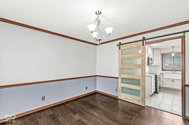 unfurnished room with a barn door, ornamental molding, wood finished floors, and a notable chandelier