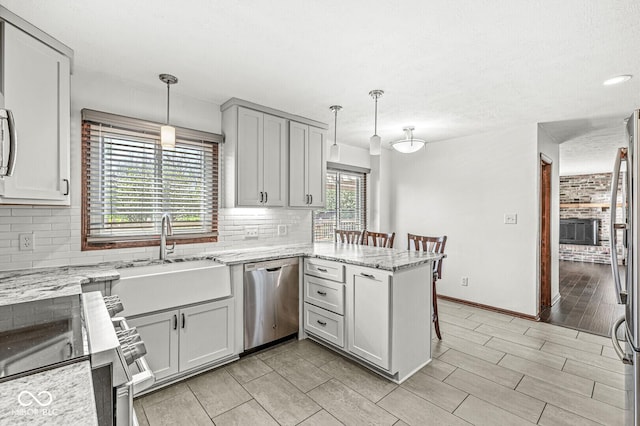 kitchen featuring a peninsula, light stone countertops, tasteful backsplash, a sink, and appliances with stainless steel finishes