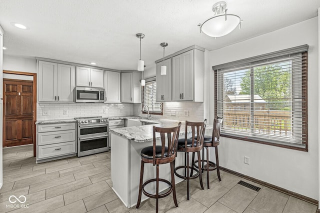 kitchen with stainless steel appliances, gray cabinetry, and a peninsula