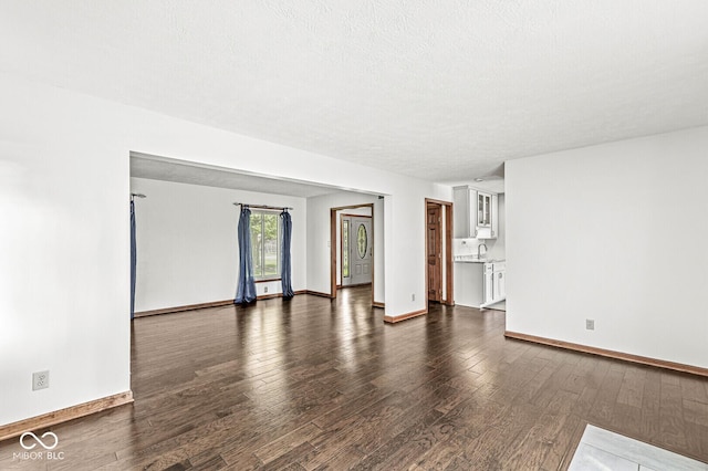 unfurnished living room featuring a sink, baseboards, and dark wood finished floors