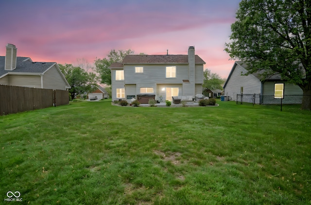 back of property at dusk with a lawn, fence, and a chimney