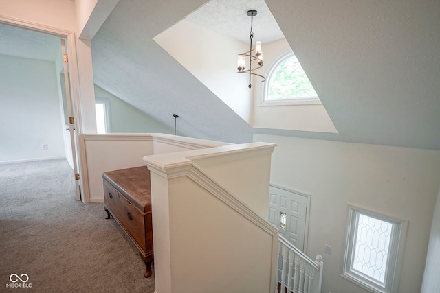 hallway featuring a notable chandelier, lofted ceiling, carpet, and an upstairs landing