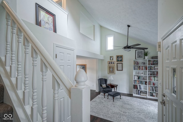 stairs with ceiling fan, a textured ceiling, wood finished floors, high vaulted ceiling, and baseboards