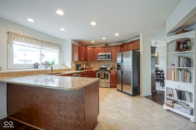 kitchen with a peninsula, light stone countertops, recessed lighting, a sink, and stainless steel appliances