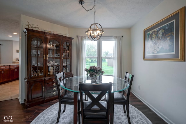 dining room with baseboards, a textured ceiling, dark wood-style flooring, and a notable chandelier
