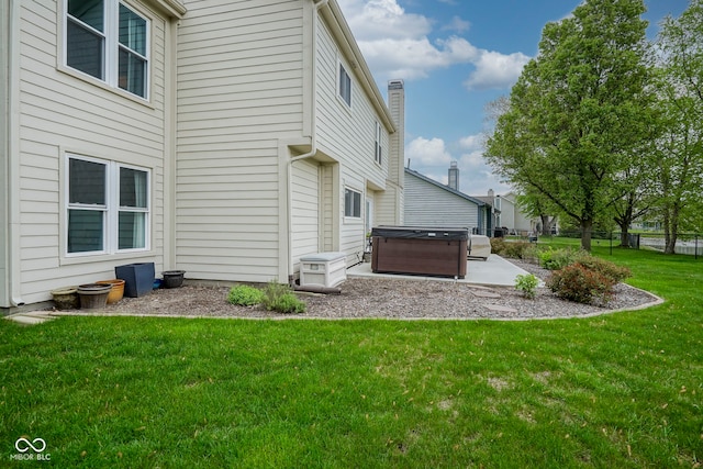 back of property with fence, a chimney, a patio area, a lawn, and a hot tub