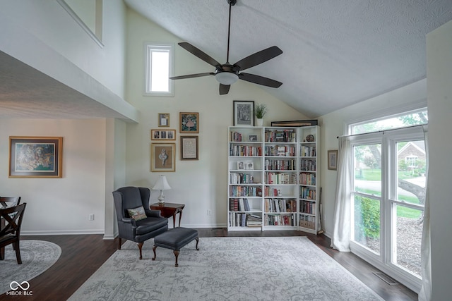 living area with a ceiling fan, a textured ceiling, dark wood-style floors, and baseboards