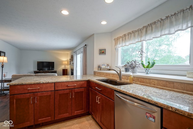 kitchen featuring a peninsula, open floor plan, light stone counters, a sink, and dishwasher