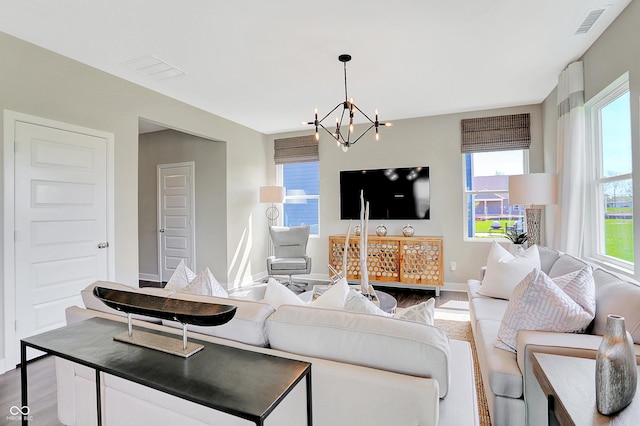 living area with an inviting chandelier, baseboards, wood finished floors, and visible vents
