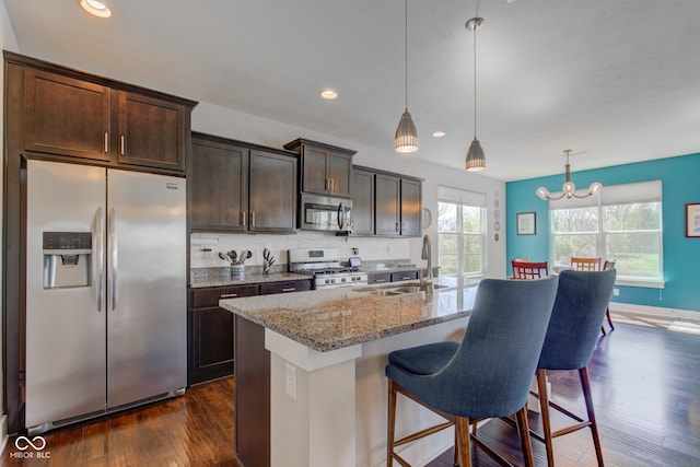 kitchen with dark brown cabinetry, light stone counters, a sink, a breakfast bar area, and stainless steel appliances