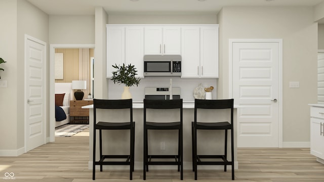 kitchen with light wood-type flooring, stainless steel microwave, range, and a kitchen bar