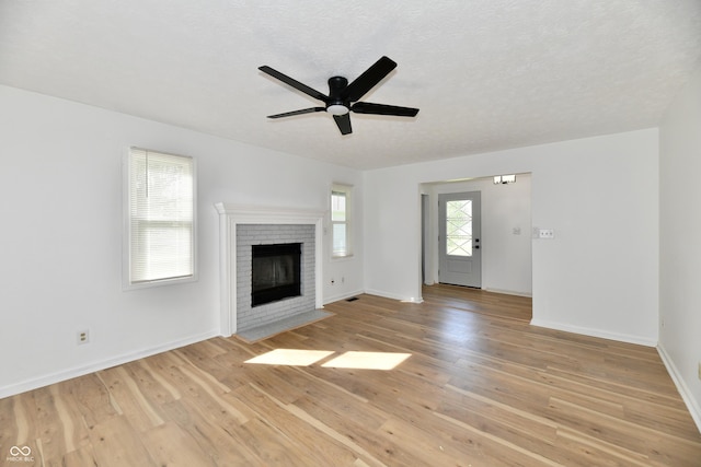 unfurnished living room featuring a brick fireplace, ceiling fan, baseboards, and light wood-type flooring