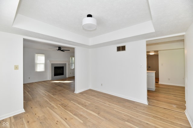 unfurnished living room featuring light wood-style floors, a tray ceiling, a brick fireplace, and visible vents